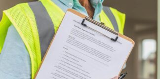 Person in yellow reflective safety vest holding a pen and checklist of house inspection