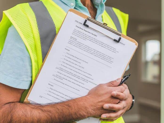 Person in yellow reflective safety vest holding a pen and checklist of house inspection