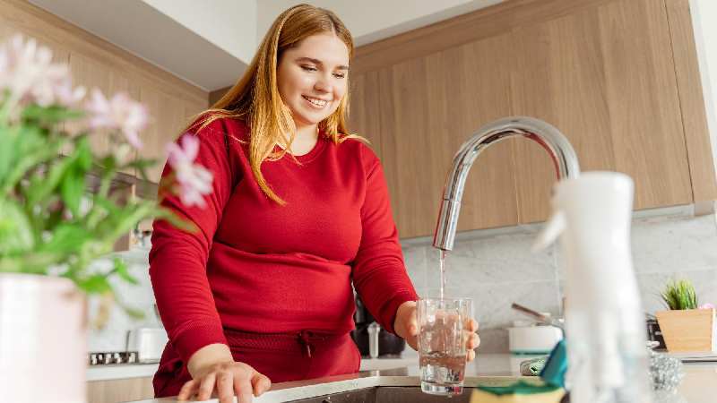 Woman in red clothes pour water from faucet in kitchen