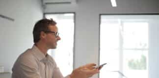 3 Types of Beneficial Programs You Should Implement in Your Company Smiling man using cell phone in the office